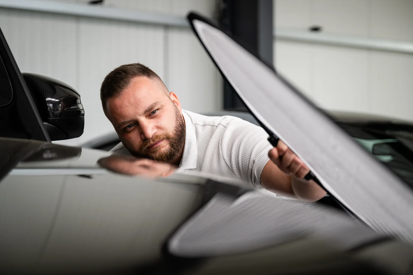 Sachverständiger bei der Nahinspektion eines Fahrzeugschadens mit Lackspiegel